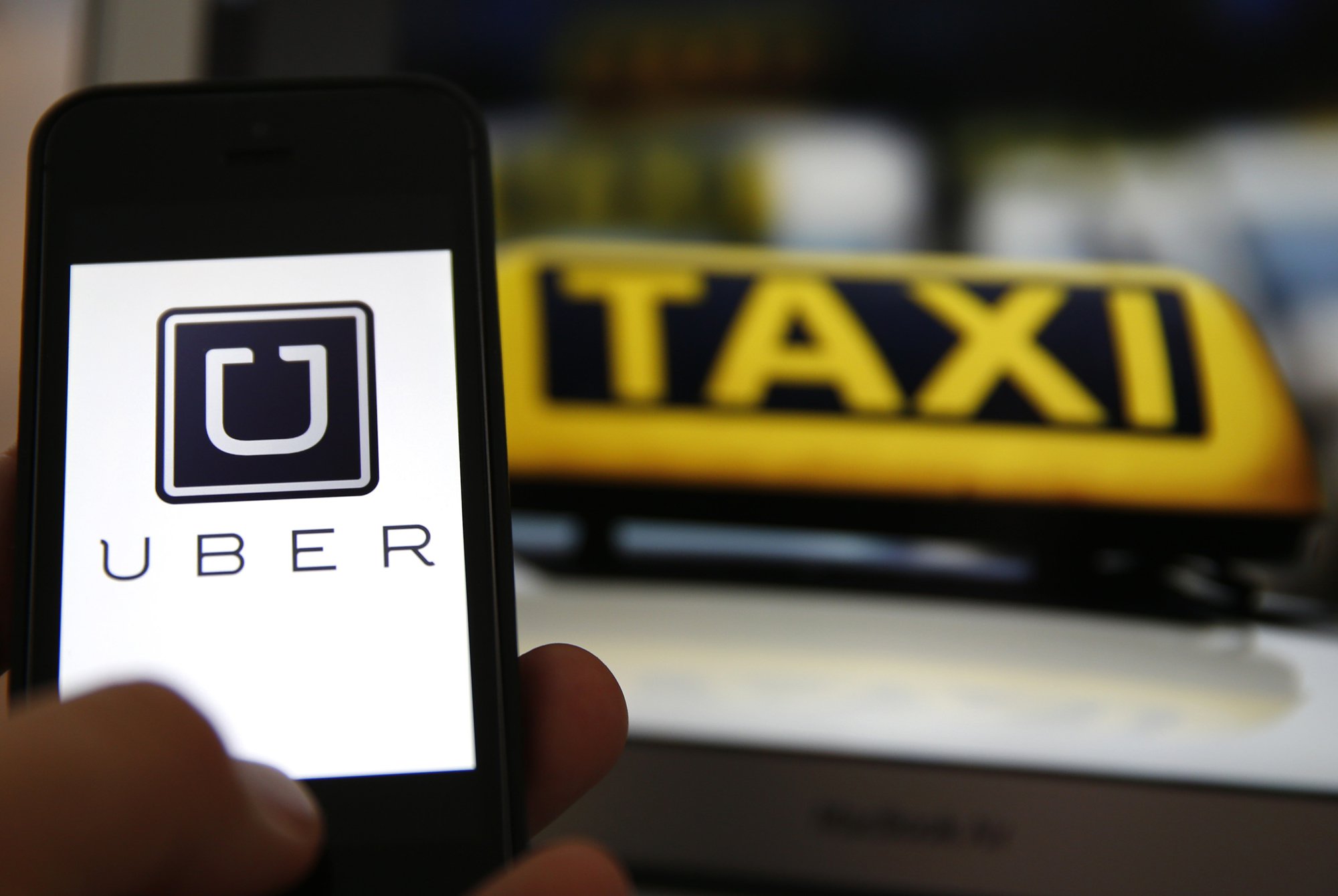 File illustration picture showing the logo of car-sharing service app Uber  on a smartphone next to the picture of an official German taxi sign -  SecureNews